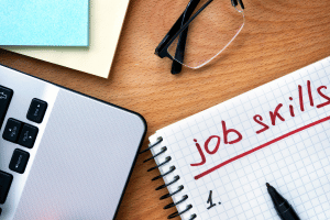 Job skills written on graph paper with 1. computer, glasses and paper on table